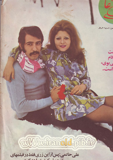 The image is a vintage magazine cover featuring a man and a woman posing for the camera. The man is on the left and the woman is on the right, both sitting in the snow. The man is wearing a striped scarf around his neck and has a curly mustache. The woman has long brown hair and a flowery dress. They're both looking at the camera with a slight smile. The text around the image appears to be in Arabic, and there's a red heart symbol in the upper right.