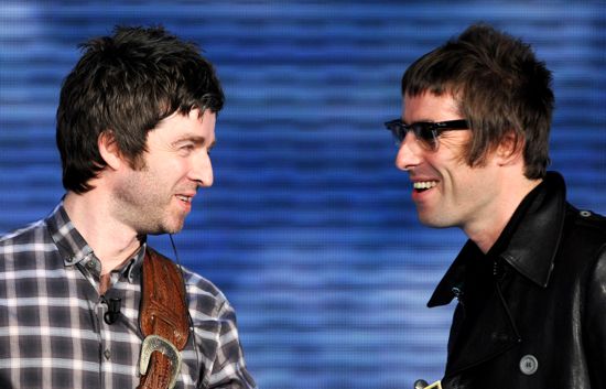 Band Ugly Member Pistonheads - The image depicts two men standing next to each other, presumably on stage or at a public event. Both men are wearing glasses and have similar eye colors and beard styles, suggesting they might be related or of the same age group. Their attire consists of casual, patterned shirts with leather details, and one man also has what could be a cigarette in his mouth. The background is abstract and lacks distinct features, directing the viewer's attention to the men. The interaction between them appears to be friendly or perhaps in the midst of a conversation, as one man is staring notably at the other.