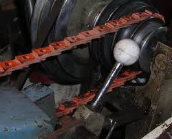 A man holding a baseball bat in his hands - Pistonheads - This image shows a close-up view of a machine, featuring a prominent metal flywheel and a silver wrench handle partially sticking out of a roughed surface. The machine is set against the backdrop of a dark, messy environment. The flywheel has multiple embedded discs attached to its edge. The wrench appears to be stuck or bent into an unusual position, contributing to the impression of an intricate mechanical device.