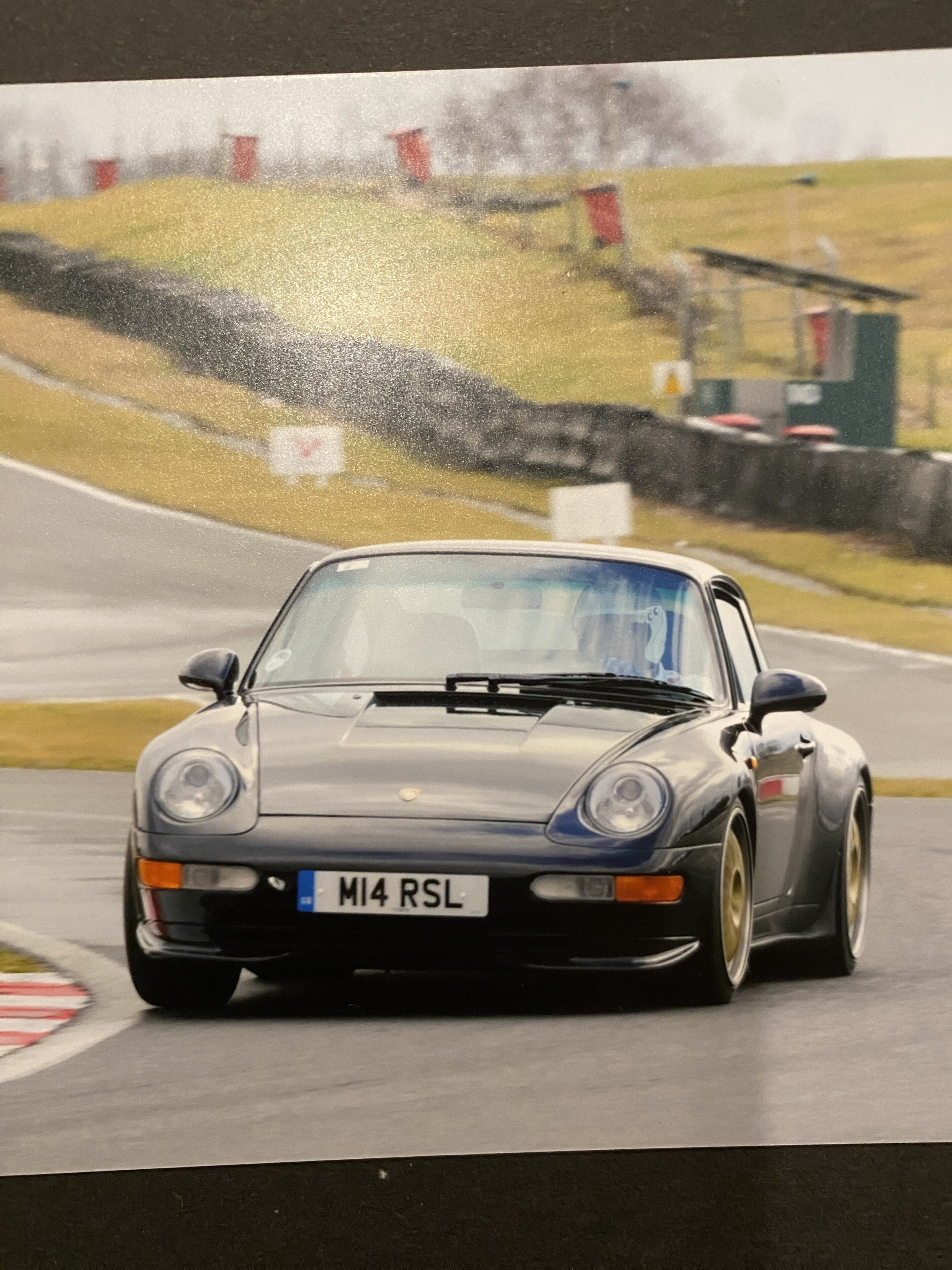 993 rs lightweight or clubsport - Page 9 - Porsche General - PistonHeads UK - The image displays a photograph of a racing car on a track. The vehicle is a Porsche, identifiable by its iconic design and the number "49" visible on the side. It's a sports car modeled as a GT3RS, equipped with a large rear wing for aerodynamic downforce. The car has the standard racing livery with sponsor logos, including "Pirelli," which is displayed prominently along the side of the vehicle. The track setting includes barriers and signs that are typical for motorsport events. The photo appears to be taken from an elevated angle, capturing a sense of motion as if the car is in the process of lapping the track.