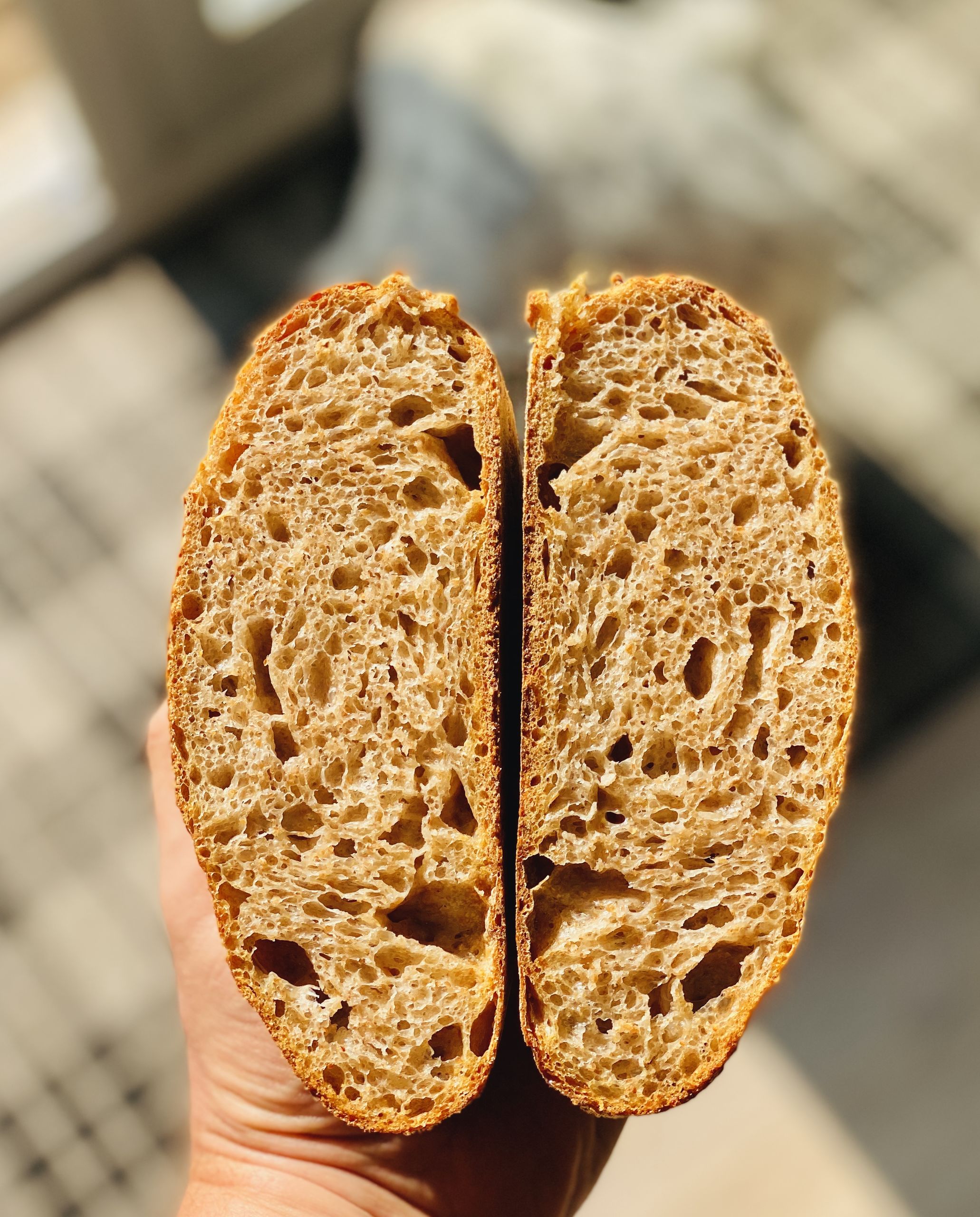 Sourdough breadmaking - Page 18 - Food, Drink & Restaurants - PistonHeads - The image shows a large loaf of bread with visible holes or seeds throughout. This loaf is placed on a surface, and there's a hand in the foreground holding two slices apart. The background appears to be an indoor setting with a window that suggests it might be a sunny day outside. There are no texts present in the image.