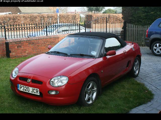 After selling the MGF, Then looking at MR2s, we bought a.... - Page 1 - MG - PistonHeads - This image features a vibrant, glossy red sports car parked on a grassy area amidst a backdrop of a brick wall and a wooden fence. The car is positioned at an angle to the viewer, highlighting its sleek design and state-of-the-art features. Its license plate reads 'P220 JCR', indicating a UK registration. The rear portion of the vehicle can be seen, complete with the iconic Bugatti emblem, adding a touch of luxury to the overall scene. The sky above is overcast, suggesting that the photo was taken during a cooler time of the day. The image conveys a sense of tranquility and a hint of the owner's passion for automobiles.