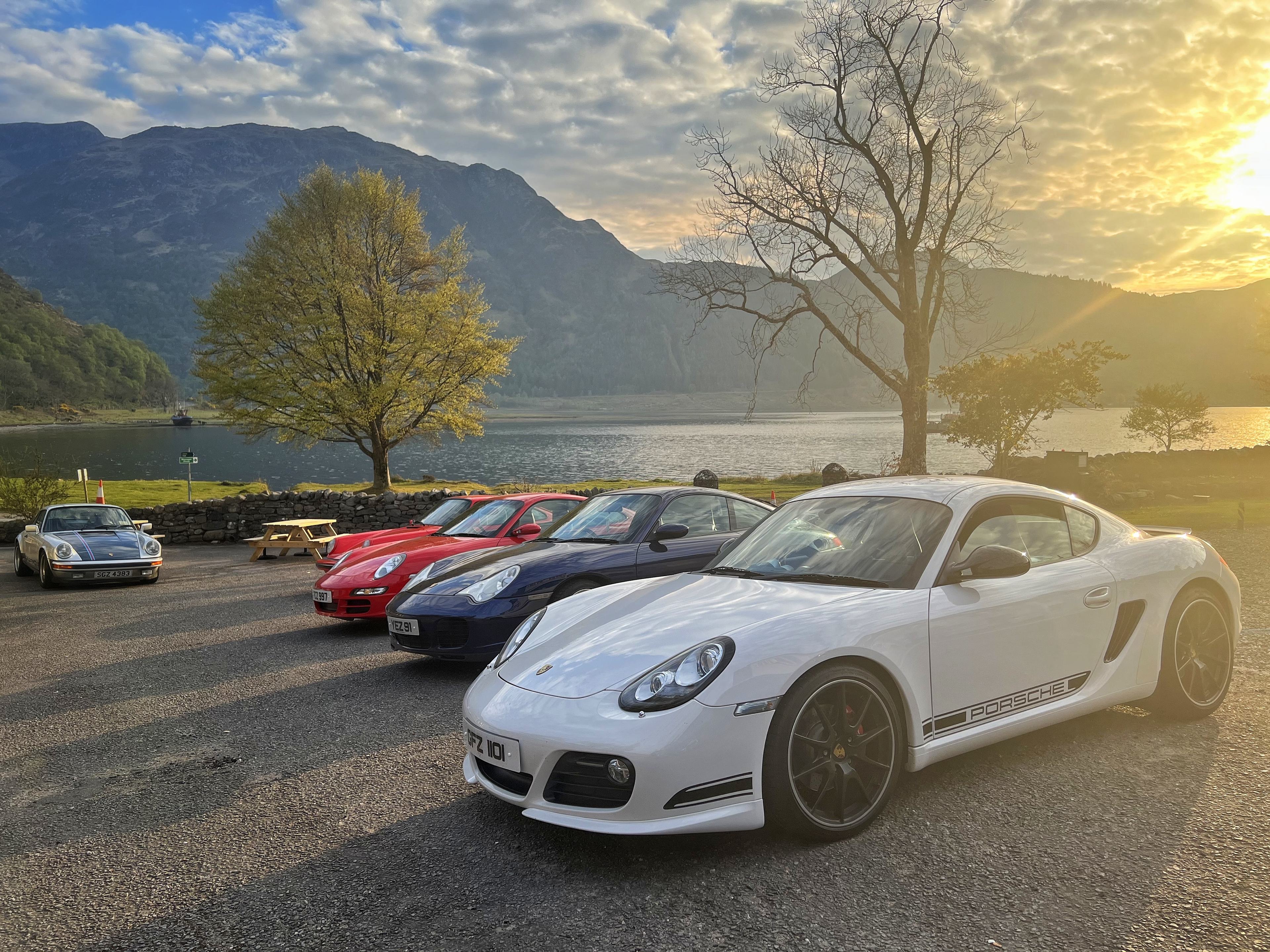 NC500 ish - Trip Report  - Page 3 - Roads - PistonHeads UK - This image captures a serene scene of a parking lot filled with luxury sports cars. The cars are parked on a gravel surface, each facing the same direction, creating a neat and orderly arrangement. There's an array of colors, from vibrant reds to sleek silvers, adding to the visual appeal of the scene. 

In the background, a tranquil lake with a mountain in the distance adds a touch of nature to this car showcase. The sky above is clear and blue, suggesting that the photo was taken during a sunny day. This image seems to be taken at either dawn or dusk, given the soft lighting that bathes the scene. 

The composition of the image suggests it might have been taken by someone interested in cars or automotive photography. The focus on the sports cars and their arrangement indicates a keen interest in automobiles. Overall, this image conveys a sense of luxury and sophistication, both through the choice of cars and the natural backdrop.