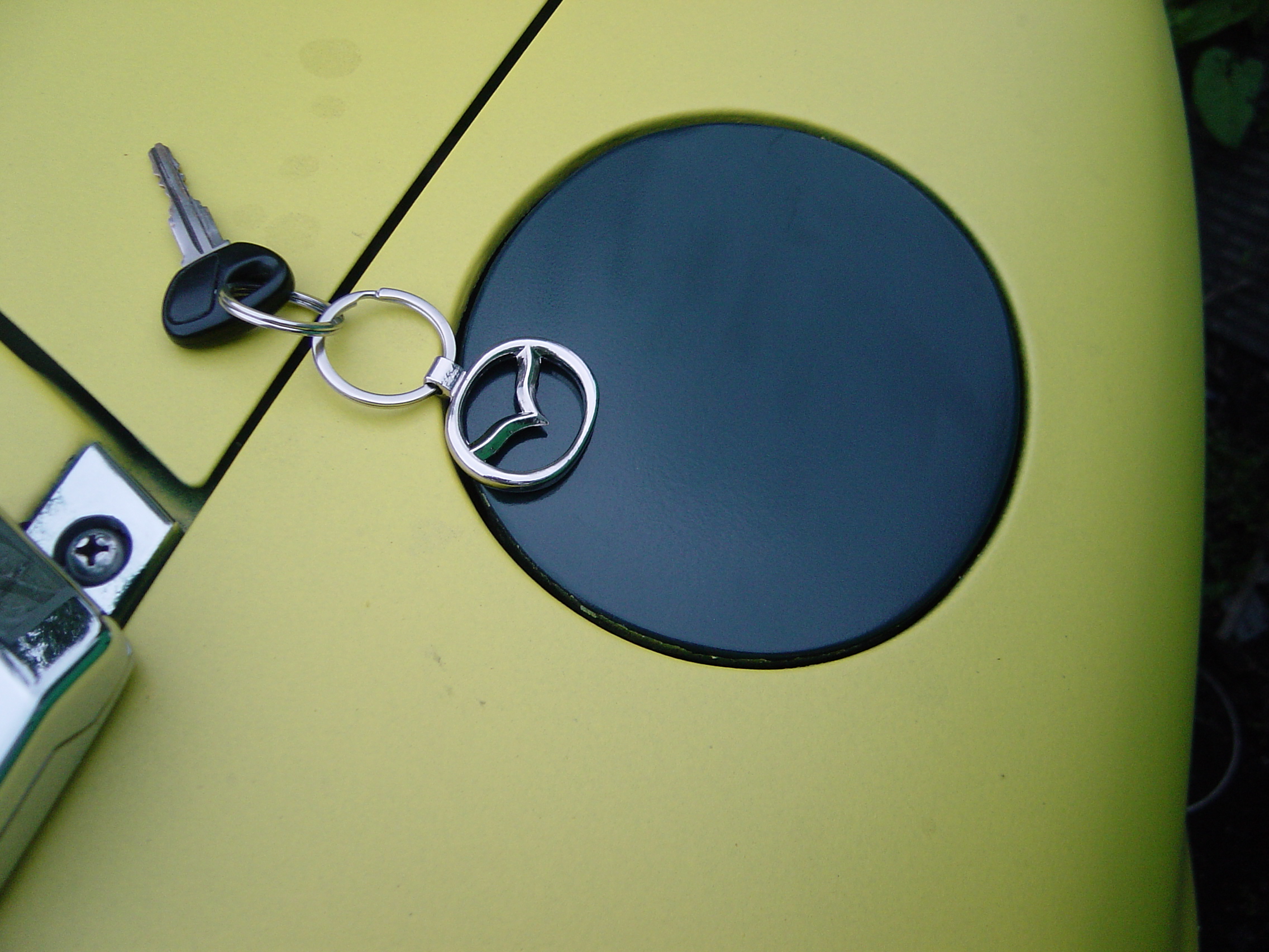 Saved from the "Scene" Mk1 MX5 rescue-ish - Page 1 - Mazda MX5/Eunos/Miata - PistonHeads - The image features a bright yellow object with a silver Mercedes-Benz emblem and a black key attached by a key ring. The emblem represents a compass, suggesting a navigation or travel theme. Adjacent to this object is a small black and white item, possibly a car lock or a component of a garage door opener. The background is blurred, emphasizing the vibrant color of the yellow object and drawing attention to its details. The focus of the image suggests it was taken with a shallow depth of field.