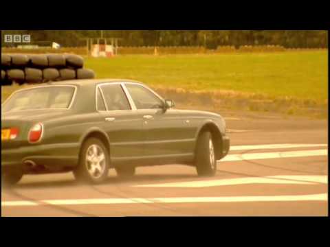 Bentley Arnage T - Page 1 - Rolls Royce & Bentley - PistonHeads - This image shows a sedimentary water course with a brown landscape on one side and a body of water on the other. The car appears to be in motion as foregrounded by the blurriness of the background and the road. The vehicle is a dark-colored sedan, possibly Volvo, with a distinctive front grille design. The surrounding environment is grainy and low resolution, which suggests the photo may have been low-quality or subject to an overlaid filter effect.