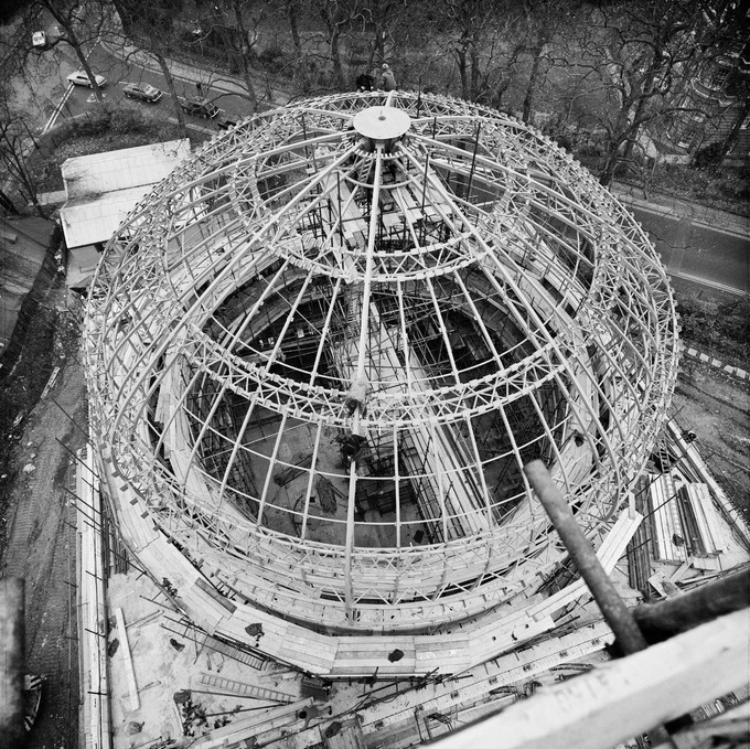 The camera can capture some fantastic moments V - Page 18 - Photography & Video - PistonHeads - The image is a black and white photograph showcasing an architectural structure. At the center of the photo, there is a large, dome-like building with intricate metalwork around its top, which forms a spherical shape. This dome is supported by sturdy metal scaffolding and features multiple layers of metal framework. The entire structure is encased in a transparent material that allows for visibility inside the sphere. Surrounding this central structure are various other elements like buildings, trees, and a fence, indicating an urban or semi-urban setting. There's a sense of scale and complexity as the photograph captures both the grandeur of the central dome and the context in which it is placed.