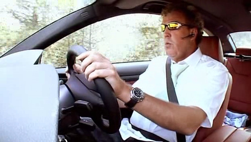 Pistonheads - The image shows a man in the driver's seat of a vehicle. He is wearing a white shirt and it appears he is in motion in the car, as the surroundings outside the car suggest speed. The man's face is slightly obscured by a pair of sunglasses that he is wearing, and he seems to be looking forward at the road ahead. The interior of the car is partially visible, showing the dashboard area with a steering wheel. The car's design suggests it may be from the 2000s, and the driver seems to be seated comfortably and is driving with both hands on the wheel.