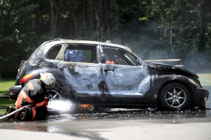 PT CRUISER Infernal dinging warning noise. How do I kill it? - Page 1 - General Gassing - PistonHeads - In the image, there is a black car parked outside, appearing to be in a burned state with its sides charred and flames still visible. The car is parked near a line of trees and what appears to be a fire hydrant. In front of the car, there is a figure in a firefighter uniform, positioned closer to the bottom of the image, seemingly extinguishing or inspecting the car. The smoke and fire suggest that the car has been either involved in an accident or deliberately set ablaze. The image captures an unusual scene, as it is not common to see vehicles on fire in this context.