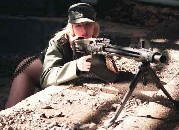 Girl Gun - The image depicts an individual from the back, wearing a military-style uniform and a cap, kneeling on the ground with a rifle. It's taken in a setting that appears to be an underground or underground-like location. The uniform indicates a possible connection to the military or a special forces unit. The overall atmosphere of the photograph is mysterious and dramatic, with subdued colors and shadows that add to the intrigue of the scene.