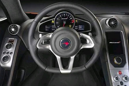 dash again - Page 1 - Ultima - PistonHeads - The image captures a luxurious car interior, focusing on the steering wheel and its surrounding features. The steering wheel is black with red highlights and a red logo in the center. 

The car dashboard, which is predominantly black, is equipped with advanced technology. The design is sleek and modern, with crisp technical displays and controls.

On the left side of the steering wheel, there's a gear shift indicator, adding to the car's high-tech appearance. The overall impression is of a vehicle that combines style with function, offering the driver a commanding view and intuitive controls.