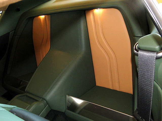 Pistonheads - The image captures the inside of a car, focusing on the passenger side door and seat. The seat is a light green, contrasting with the cream-colored side panels. These panels are adorned with a vertical quilting design, adding a touch of luxury to the car's interior. The door, featuring a black handle and matching strap, opens to reveal a metal footrest, an unexpected yet functional detail. The resting angle of the photo gives a sideways perspective of the car, emphasizing the layout and design of the seats and sides.