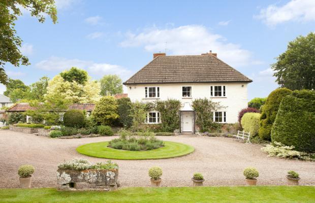 What does your house look like? - Page 8 - Homes, Gardens and DIY - PistonHeads - The image shows a large, detached house with a white facade, set in a well-maintained, landscaped garden. The property features a neatly manicured lawn with a central circular lawn and multiple potted plants placed evenly on both sides of a central path leading to the house. The house itself has dormer windows on the second floor and a white door at the center front entrance. There are also mature trees in the background, suggesting a quiet and residential area.