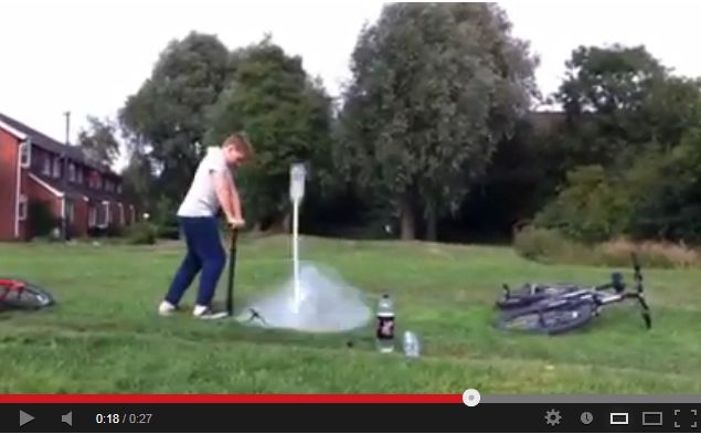 A man is throwing a frisbee in a park - Pistonheads - The image shows a person in a park or open grassy area. The individual, who appears to be a male, is wearing a light-colored sleeveless shirt and blue pants. He is standing and actively engaged with a device that emits smoke, directed towards a target he is aiming at with a device in his hands. There are a couple of bicycles lying on the ground in the background, suggesting a casual, outdoors setting. The image's style is that of a standard, unedited real-life photograph with no filters or artistic manipulations.