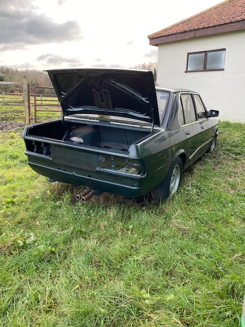 Classics left to die/rotting pics - Vol 2 - Page 329 - Classic Cars and Yesterday's Heroes - PistonHeads UK - The image showcases a vintage car, specifically a green hatchback, parked on grass. It's an old model, as indicated by the visible damage on its side. The vehicle is positioned in front of a building with a white door and a gray roof, suggesting a residential or commercial area. The car appears to be abandoned, with no immediate signs of use or maintenance. The setting suggests it might have been there for some time.