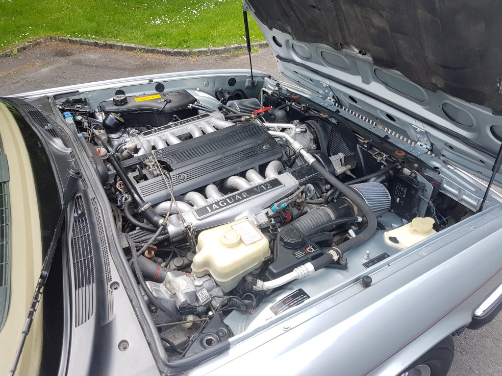 Lovely Cars: Interesting, Classic, Retro, Barge 5-10k - Page 95 - General Gassing - PistonHeads - The image shows a close-up view of the engine bay of a silver car. The engine appears to be well-maintained and is an inline four with visible components such as a fan belt, radiator, intake manifold, and filter. The radiator and fan are partially visible and seem to be in good condition, indicating the vehicle is likely in proper working order. There are no visible texts or logos in the image that provide more information about the brand or model of the car. The background is mildly out of focus, which suggests that the emphasis is on the car's engine. The overall setting appears to be an outdoor parking area.