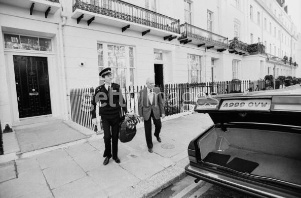 Pistonheads Classics Famous - In this vintage black and white image, two police officers are seen outside a large white building. They are dressed in uniform, each holding a handbag. The building has a black gate and a row of potted plants along the front. A distinctive feature of the car parked on the sidewalk in front of the building is a license plate that reads "A99 OWV". There's no visible activity or context provided for why the officers are at the location. The general atmosphere of the image is both formal and lawful.