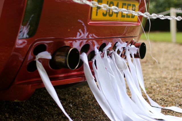 Random TVR pics - Page 369 - General TVR Stuff & Gossip - PistonHeads - The image showcases a red car parked on a gravel driveway. Notably, the car has a contrasting white exhaust, which is bent near the rear, creating a unique visual effect. The exhaust is enhanced by the installation of a white chain, transforming the otherwise mundane element into a striking feature. The backdrop of the setting sun complements the vibrant colors of the vehicle and the chain, adding to the dramatic appeal of the scene.