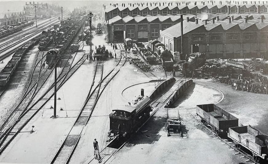 Loco sheds and other railway buildings... - Page 37 - Boats, Planes & Trains - PistonHeads UK - The image is a black and white photograph depicting an old train yard. It features multiple trains parked on the tracks, which appear to be made of steel. In addition to the trains, there are several buildings visible in the background, one of which has the letters "RAM" prominently displayed. The setting appears to be a bustling industrial area with a significant amount of infrastructure related to rail transport. There are no people visible in the image. The photograph captures a moment in time, likely from the early 20th century judging by the style of the trains and the buildings. The monochrome tone adds a sense of nostalgia and history to the scene.