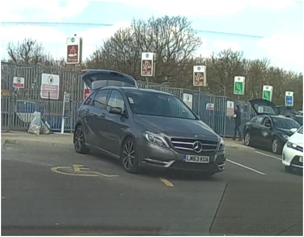 The BAD PARKING thread [vol3] - Page 463 - General Gassing - PistonHeads - The image captures a scene with multiple vehicles parked in lots. The most prominently featured vehicle is a dark Mercedes-Benz car, parked close to the viewer. In the background, a variety of cars and trucks fill the lots, displaying a variety of colors and models. The setting seems to be a busy commercial area with many signs visible. The overall impression is of a bustling parking lot during daylight hours.