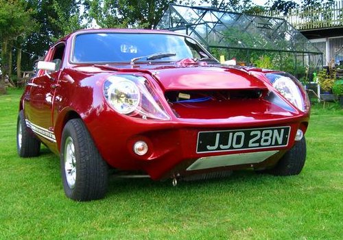 A vintage car is parked in a field - Pistonheads - The image shows a vibrant red sports car parked on a neatly mowed lawn. Its shiny exterior gleams under the light, highlighting the various curves and angles of the vehicle. The car is equipped with alloy wheels, adding to its sporty appeal. The license plate reads "JJO 28N", suggesting the car's unique characteristics. The car is parked in front of a white metal fence, indicating a residential or private property.