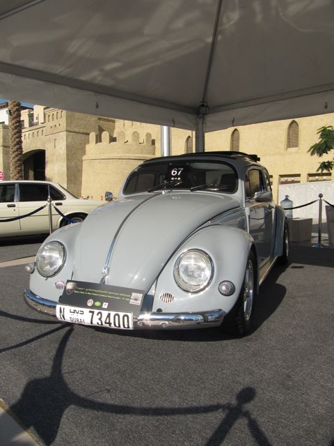 Classic Pistonheads Emaar - The image showcases a vintage Volkswagen beetle, a classic symbol of the mid-century automotive design. The car is painted in a clean off-white color and is equipped with what appears to be a sunroof. It's parked under a canopy, possibly at an auto show or a similar event, given the presence of a rope barrier around the vehicle. The car is positioned in front of a beige-colored building with an imposing castle-like structure, adding a unique contrast to the vintage vehicle.