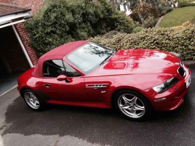 Show Me Your BMW!!!!!!!!! - Page 280 - BMW General - PistonHeads - The image features a red BMW sports car parked on a driveway. The car is sleek and glossy, reflecting the sunlight, and it's positioned at an angle with its left side visible. The driveway is partially paved with concrete and partially covered in gravel. The car is parked next to a house with a brick facade, and there's lush greenery in the background, providing a serene ambiance.