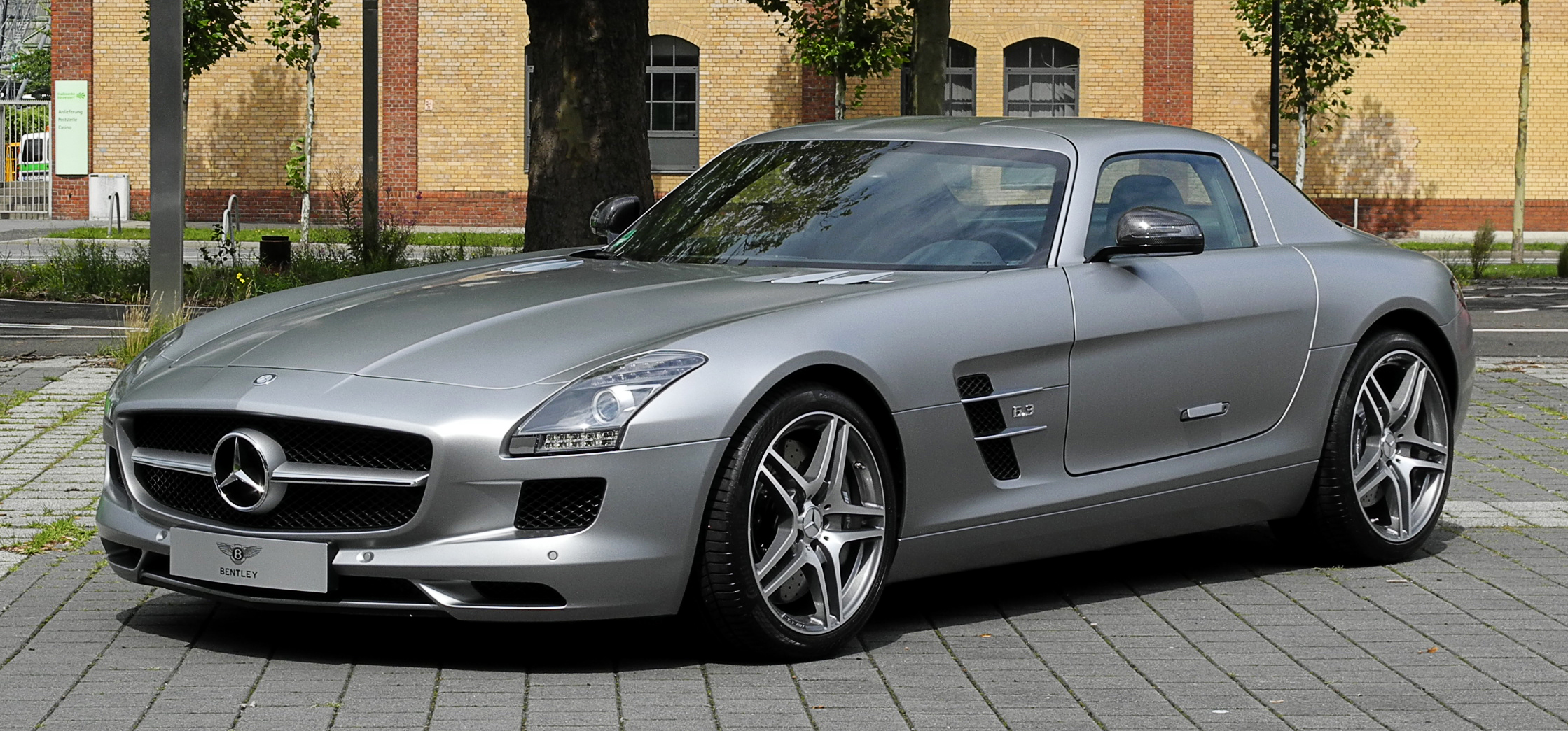 Ugly beautiful cars - Page 4 - General Gassing - PistonHeads - This image shows a sleek silver vehicle parked next to a street. It appears to be a Mercedes-Benz, as indicated by the grille and the distinct style of the car. The vehicle is viewed from a three-quarter angle, highlighting its aerodynamic design and the alloy wheels. The background consists of a paved road and a building with brick walls and a flat roof. There is no visible text or distinctive branding. The overall atmosphere of the image is clean and modern, suggesting a metropolitan or urban setting.