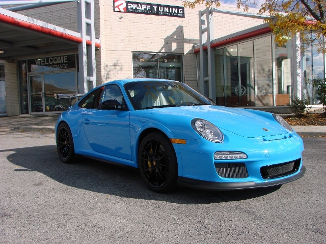 Spray Job & interior Recolour (Co Durham Area) - Page 1 - Porsche General - PistonHeads - The image features a bright blue Porsche sports car parked in front of a building with large glass windows. The vehicle, facing towards the camera, has a sleek design with alloy wheels, and its hood features the distinctive Porsche emblem. The car is positioned on an asphalt surface, and the building in the background prominently displays signs, indicating it might be a business establishment. The overall scene suggests an urban or commercial setting.