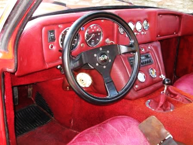 Early TVR Pictures - Page 28 - Classics - PistonHeads - The image depicts the interior of an old red car, possibly a convertible. The steering wheel is prominently displayed, and there are several gauges and temperature controls mounted on the steering column. Two side view mirrors are fitted on the outside of the car. The dashboard has a cluster of buttons and gauges, indicating a vehicle designed for better visibility and control of various in-car systems. The car's interior is predominantly pink and red, giving it a vintage and colorful look.