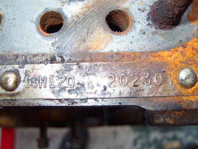 Pistonheads - The image shows a close-up view of a part that appears to be attached to a larger assembly. This part features multiple holes, possibly for bolting or attaching another component. The paint is coming off the metal, revealing the bare material underneath, indicating signs of wear or age. The area around the holes and the paint is rusted, suggesting corrosion or exposure to elements that have caused the paint to deteriorate. There's a visible number and text, indicating some form of identification or serial number, but it is slightly obscured. The style of the image is a detailed and focused photograph, emphasizing the textures and patterns in the rusted metal.