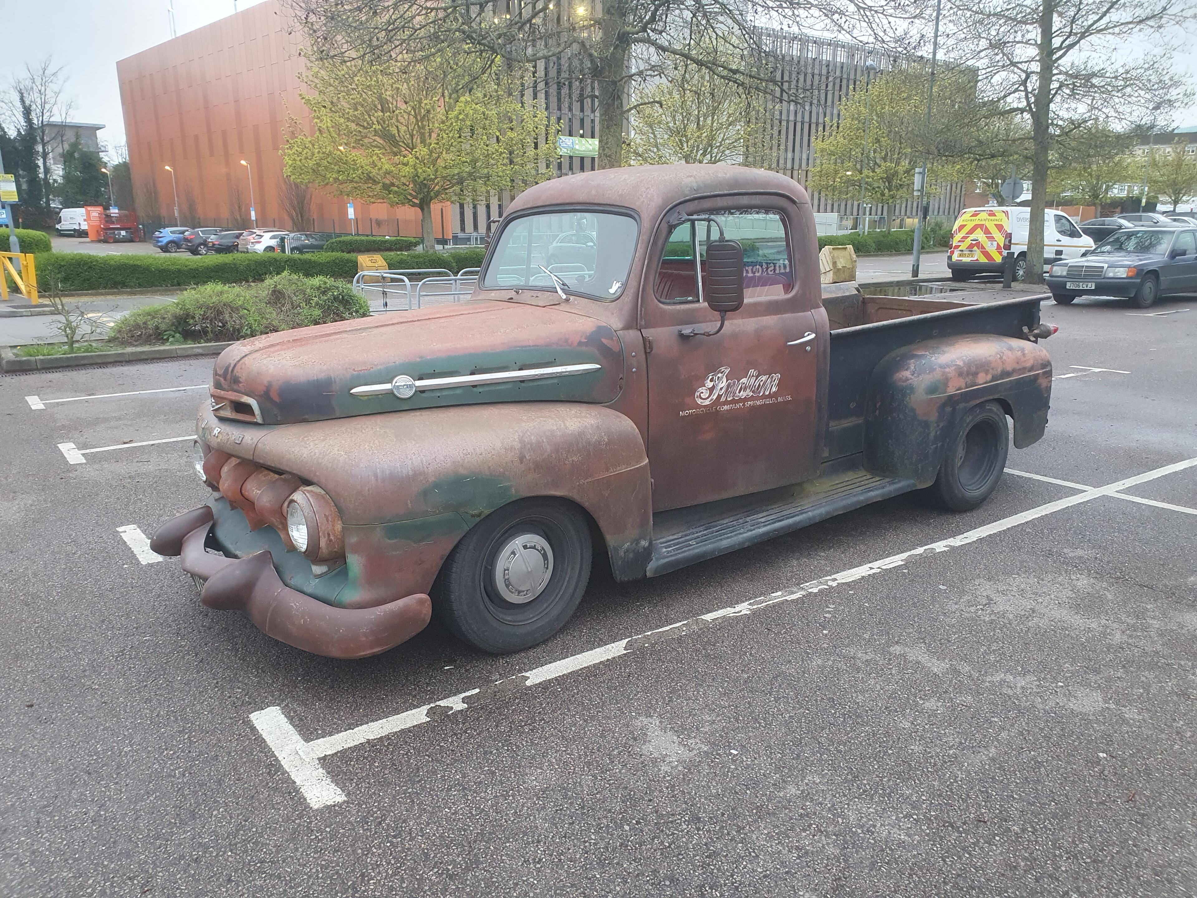 American Cars Spotted - Page 1 - Yank Motors - PistonHeads UK - The image shows an old, rusty pickup truck parked in a parking lot. It is predominantly brown with patches of rust visible on the body. The vehicle has a prominent grille and large headlights, suggesting it could be a model from the mid-20th century. On the side of the truck, there appears to be a faded advertisement or emblem. In the background, there are other vehicles parked in the lot, indicating that this is a public parking area. The style of the image is a standard photograph with no visible filters or artistic manipulations.