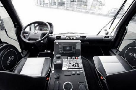 Black Pistonheads Unimog Edition Amg - The image showcases the interior of a bus, interior of the bus is black. The bus has multiple screens, one that stands out at the center. The space is well-organized and appears to be for a professional or service-related purpose. The seats suggest that passengers can adjust their position. A leather steering wheel is visible at the side.