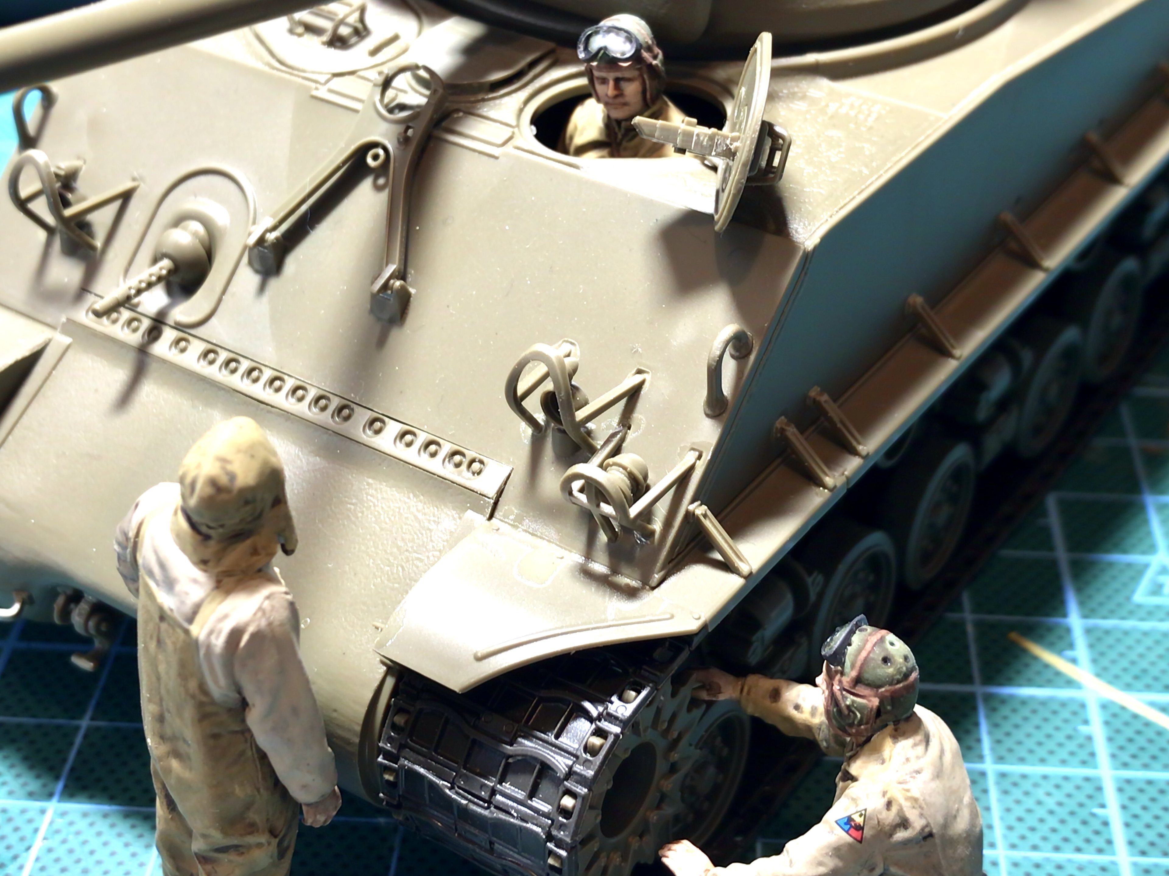 The thread where we can talk about painting figures. - Page 6 - Scale Models - PistonHeads UK - This image is a collage featuring an intricate diorama or model military scene. At the top, there's a large, detailed tank with its hatch open, revealing two figures inside; one is driving and the other appears to be working on something within the tank. Below this, there are two smaller scenes: one shows two soldiers in front of the tank, possibly discussing tactics or observing their surroundings, while the other depicts a soldier standing beside it, looking at a map or blueprint. The figures are meticulously crafted, with attention to details such as uniforms and equipment. The background is minimalistic, highlighting the precision and detail of the model scene.