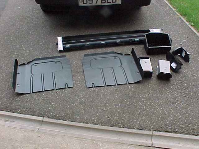 Advice Pistonheads Purchase - The image portrays a scene on a driveway where a vehicle bumper has been split into its individual parts. The bumper is laid out flat, revealing its internal structure. Alongside the bumper, are the separate components that make up the unit - each of which shows signs of detachment from the main structure. The picture appears to capture a moment of disassembly or perhaps the aftermath of an accident. The clean asphalt of the driveway provides a stark contrast to the processed, mechanical elements of the bumper and its pieces.