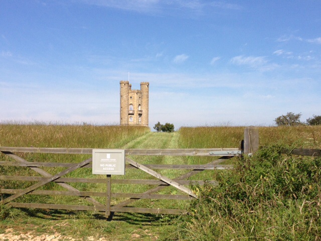 The "Photos From Today's Ride" thread... - Page 150 - Pedal Powered - PistonHeads - The image portrays a serene countryside scene. Dominating the landscape is a large castle or tower, constructed from brick, standing closely to a well-maintained wooden gate. The gate provides access to a path that gently curves towards a small tree and then onwards to a hedge along the far side of the image. The sky above is a clear blue, suggesting a bright, sunny day. The ground is grassy, and a few small bushes can be seen in the foreground. The contrast between the man-made structures and the natural landscape creates a peaceful coexistence between the past and the present.