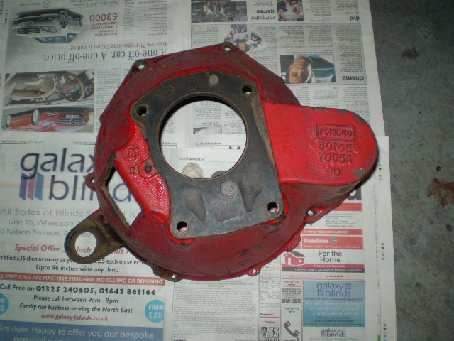 Bell Housing Pistonheads Ford - The image features a damaged red clutch framed against the background of an open newspaper. The clutch, which appears to be a part from a vehicle, has its outer red sheen blemished with patches of exposed metal, revealing a contrasting silver hue. The newspaper it lies against contains various ads and text, with a headline that reads "Galaxy.com". On the lower right corner of the photo, a partial view of a mobile phone can be observed. The newspaper appears to be dated and may be expressing sentiments toward a news organization or a specific event.