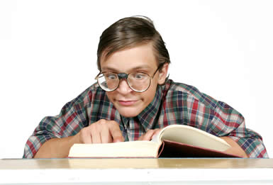 Pistonheads - The image shows a young man with a grimacing expression, looking down at a book with an intense and focused gaze. He is wearing large, round glasses and a patterned, plaid shirt. His posture leans forward over a desk or table where the book is open. The background is nondescript and does not distract from the man and his book. The overall impression is of someone deeply engrossed in their reading.