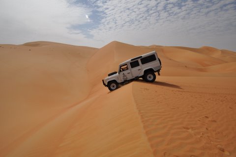 Best desert safari out of Dubai? - Page 1 - Middle East - PistonHeads - This image captures a scene of adventure and exploration. A white jeep, with its large wheels and tinted windows, is tackling the steep, sandy face of a giant sand dune. The landscape is dominated by the vast expanse of sand, undulating with the easy grace of a desert night. Above, the sky is painted with soft, diffused tones, suggesting either the crescent of dawn or the shy face of dusk. In the top left corner of the picture, a small patch of sky peeks through, stark and uncompromising in its contrast to the sandy expanse. The entire scene is bathed in a soft, golden light that casts gentle shadows and accentuates the dune's luxurious granular texture. This image truly encapsulates the thrill and allure of desert exploration.