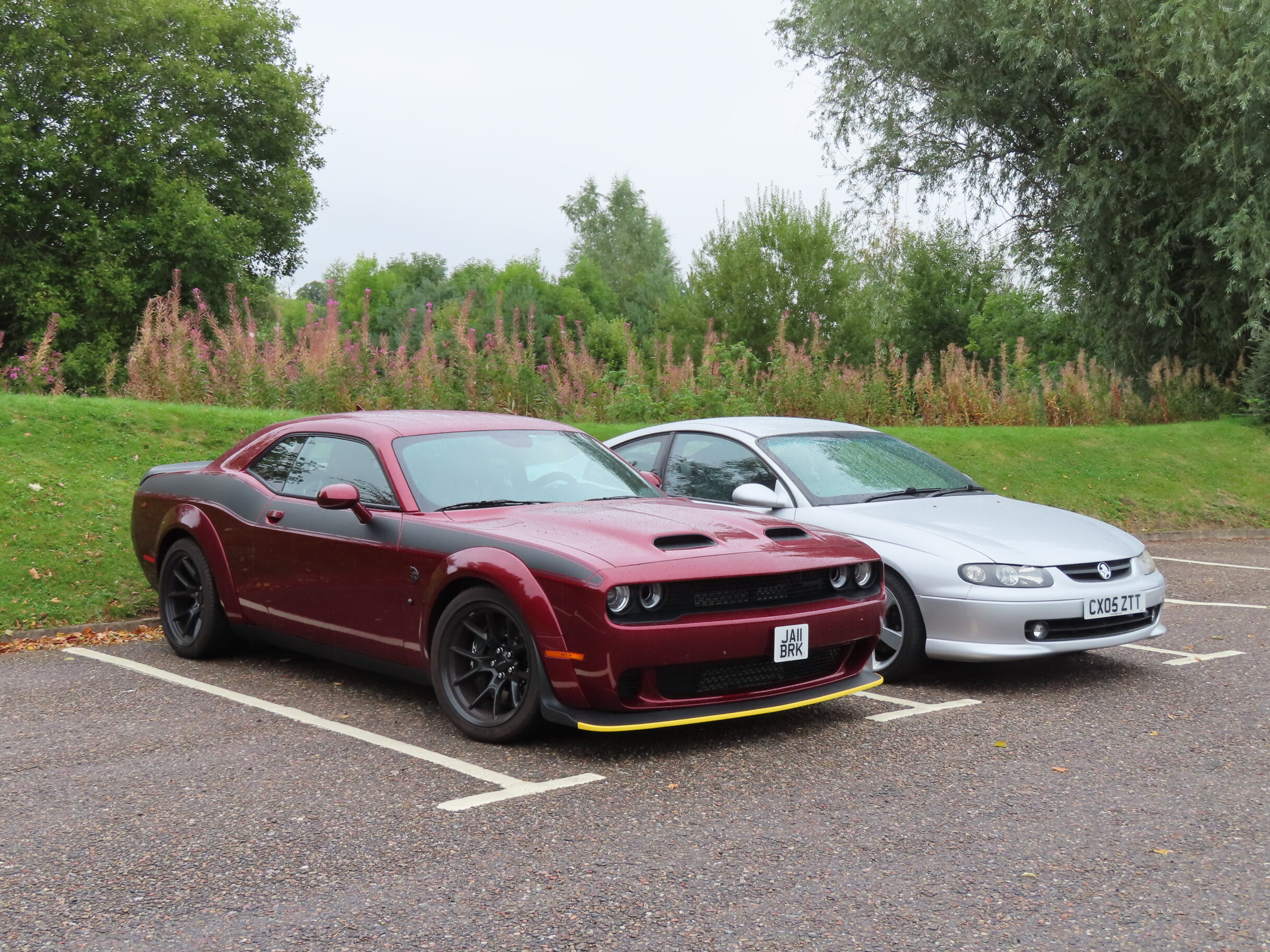 Pistonheads - The image shows two classic Mustang cars parked side by side in a parking lot. They are red and feature racing stripes, which add to their sporty appearance. Both cars have been modified with aftermarket parts and accessories, such as spoilers and rims. In the background, there is a grassy area and what appears to be a cloudy sky. The scene conveys a sense of camaraderie among car enthusiasts.