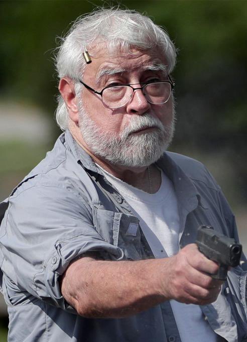 Protesters blocking various M25 Junctions - Page 333 - News, Politics & Economics - PistonHeads UK - The image is a photograph of an elderly man with white hair, wearing glasses and a cap. He appears to be in mid-speech or making an announcement, as suggested by the open microphone he holds close to his mouth. His attire suggests that he might be at an outdoor event, possibly in a park or similar setting. The man is gesturing with his right hand, holding a microphone with both hands, indicating he's addressing an audience. There are no other people visible in the background, and there is no text present on the image.