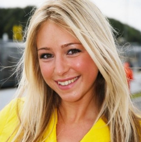 A woman wearing a blue shirt and a red tie - Pistonheads - The image shows a person with blond hair and a radiant smile. They are wearing a yellow top and appear to be indoors near an area with greenery, possibly a window overlooking gardens or a park. The person's pose and the bright place they are in create a cheerful atmosphere.