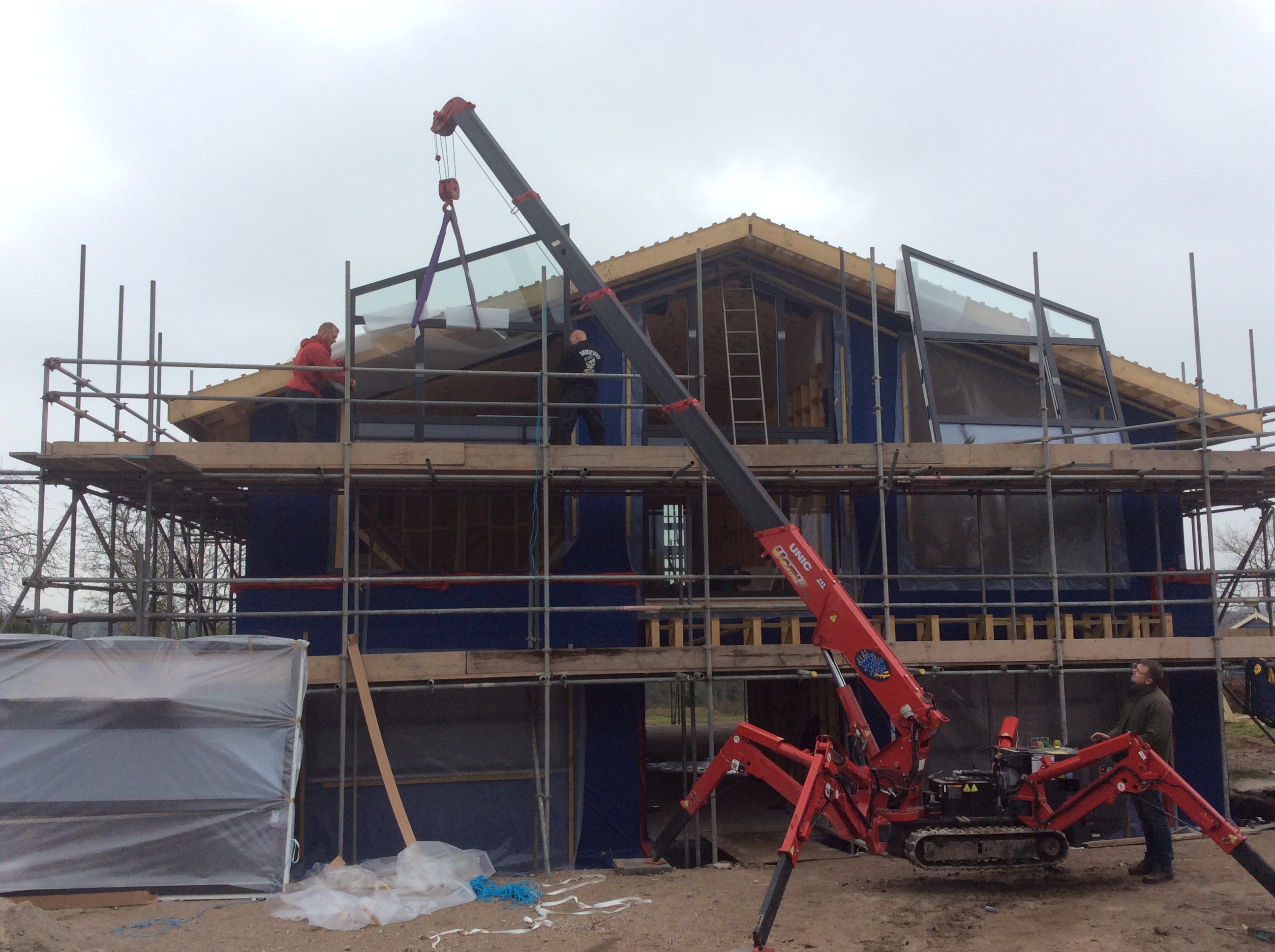 www's new build thread - Page 8 - Homes, Gardens and DIY - PistonHeads - The image features a construction site where a crane is being used. Two individuals, possibly construction workers, are present near the building. Construction materials such as scaffolding and canvas are in use, and part of the facade of the building is covered with plywood. The sky is grey, suggesting overcast weather conditions, while the surrounding environment appears to be cleared for the construction project.