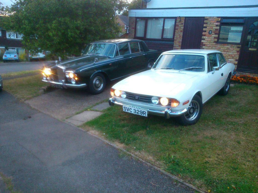 Lets see a picture of your classic(s) - Page 272 - Classic Cars and Yesterday's Heroes - PistonHeads - The image shows two vintage cars parked on a lawn in front of a building. The car on the left is a black classic model, while the car on the right is a white classic model, both equipped with round headlights. In the background, there's a driveway leading to the building. The scene also includes a small section of a sidewalk adjacent to the lawn. The setting suggests a private or residential area.