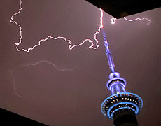 Pistonheads Lightning - The image captures a dramatic scene in Sydney, Australia, where a purple-hued tower lies in the foreground. Behind the tower, the sky is filled with dark clouds that have been struck by a bolt of lightning. The lighting from the sky illuminates the tower, casting a blue glow on it and adding to the sense of drama and power. The image conveys a sense of both tranquility and dynamism, as the tower stands still under the tumultuous sky.