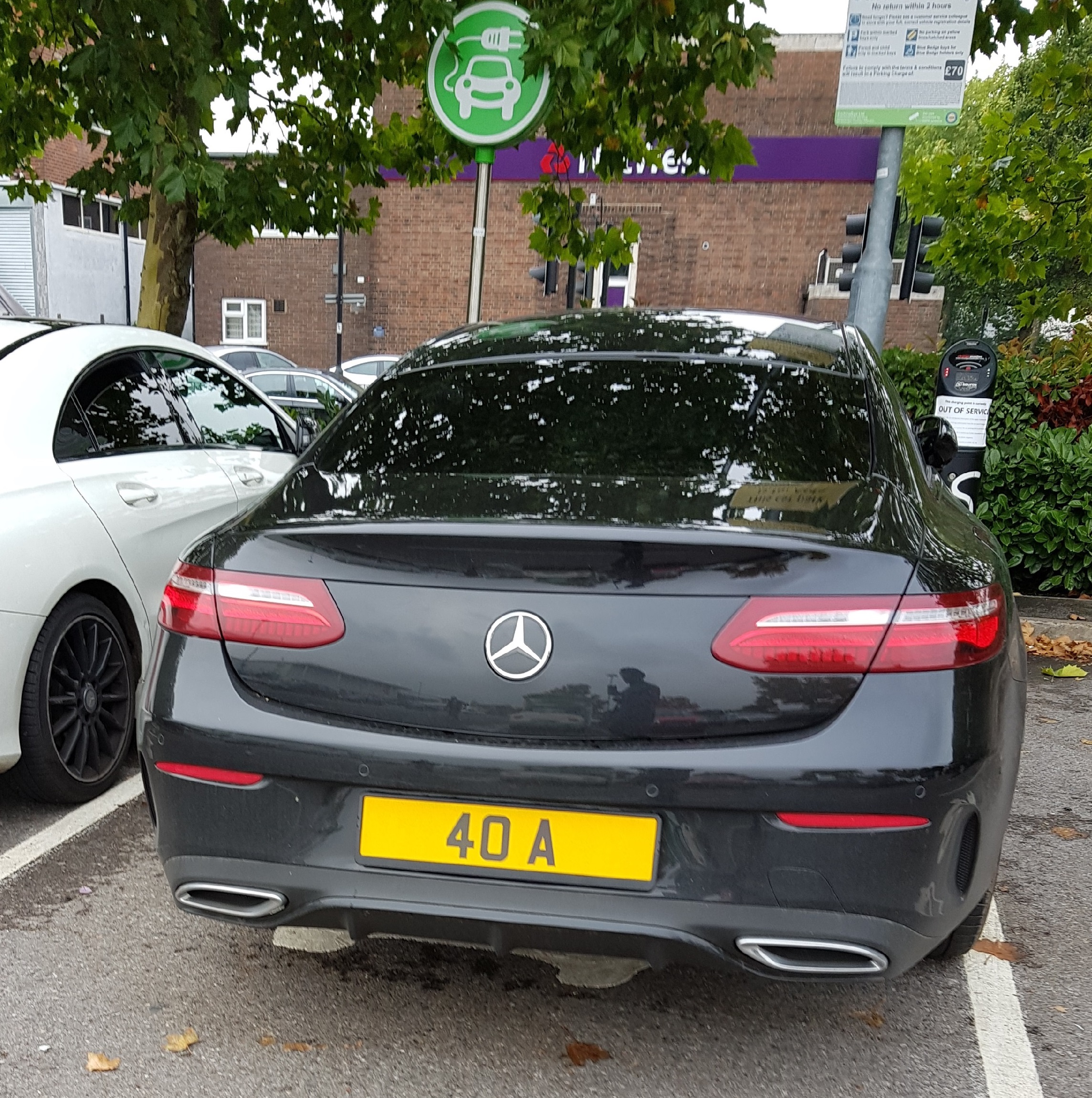 Real Good Number Plates vol 5 - Page 121 - General Gassing - PistonHeads - The image showcases a sleek black Mercedes-Benz parked in a lot, prominently displaying a yellow license plate that reads "40 A". The car is adorned with a green charging emblem, suggesting that it is electric. The background reveals the presence of a building featuring a purple awning. The setting is bathed in natural light, hinting at favorable weather conditions.