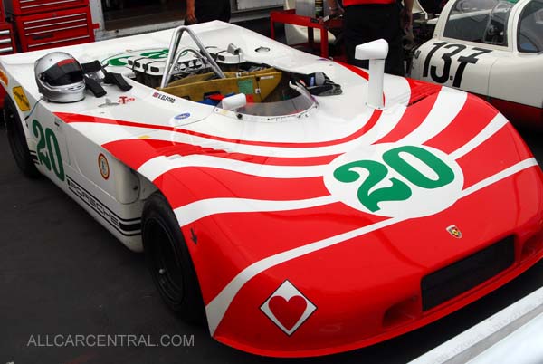 Pistonheads - The image showcases a vintage race car that exudes a sense of speed and nostalgia. The car's design features a bold red and white striped body, with additional touches of green and white. The number '20' prominently displayed on the front indicates the car's racing status. The setting appears to be a track, with other race cars visible in the background, suggesting a racing event or garages.