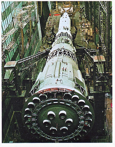 Fly to the moon for £100 million - Page 1 - Science! - PistonHeads - The image shows a large, futuristic spacecraft, painted in white and red, with a complex structure that includes various compartments, mechanical components, and what appears to be a circular habitat section. The spacecraft is surrounded by advanced industrial scaffolding, indicating that it might be under construction or maintenance in a manufacturing or assembly facility. The facility's walls are made of metal panels with a greenish tint, and there are windows at various heights along the walls, allowing light to enter and illuminate the interior components and compartments of the spacecraft. The atmosphere of the photo suggests a highly technical and advanced environment, likely a space industry or aerospace center.