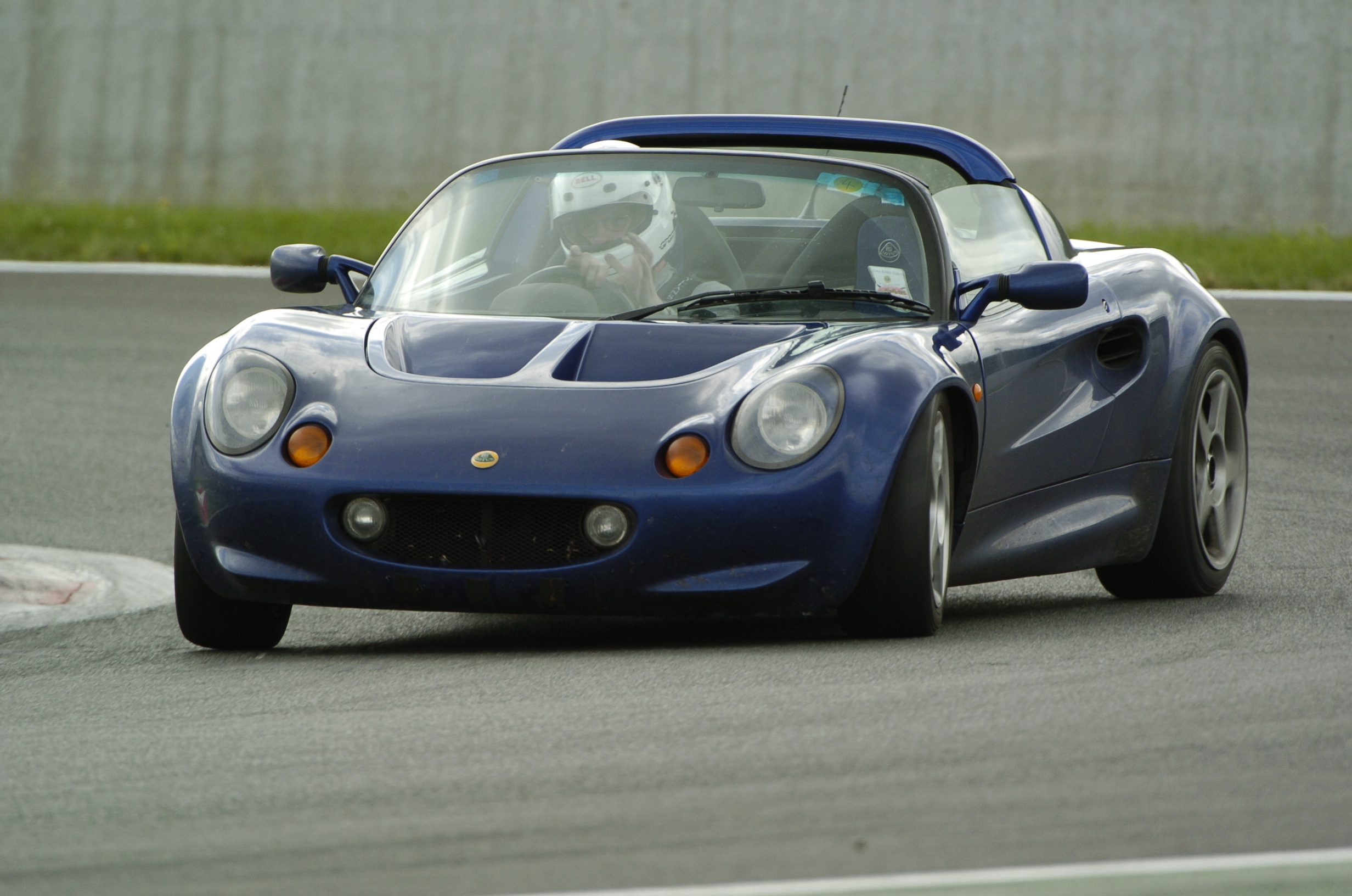 A car that is parked next to a car - Pistonheads - The image captures a blue sports car in the midst of a race track. The car, adorned with a gold emblem on the front, is painted with a sleek design and a large air intake at the back. The driver, donned in a white racing suit and a safety helmet, is inside, ready for the thrill. The car is speeding along the curved track, showcasing its agility and power. The gray sky in the background adds an element of drama to the racing scene.