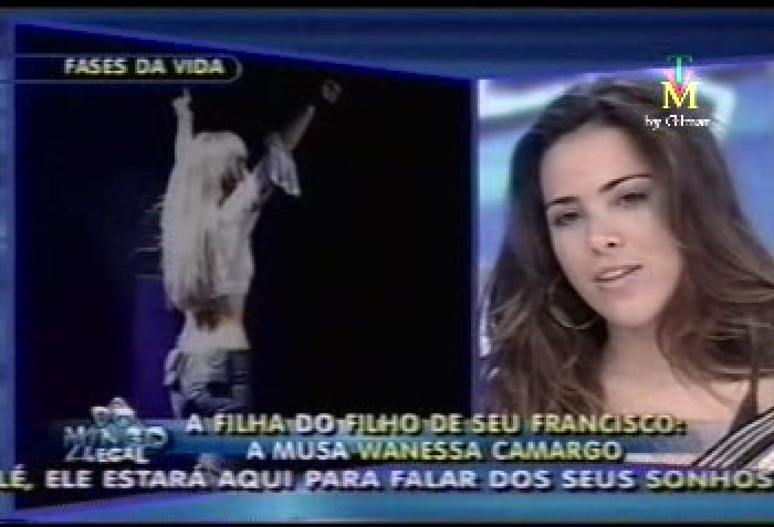 The image appears to be a screenshot from a television program, possibly a news or talk show. The central figure, a woman, is shown on the right side of the screen. She has long dark hair, is wearing a dark top, and seems to be engaged in a conversation. On the left side of the screen, a person is showing a move or performing an action, which is not clearly discernible from this angle. At the top of the image, there is a news ticker with the text "FASSES DA VIDA," suggesting that the content pertains to the repercussions of the disappearance of a film star.

Below the main image, there is a banner with text, which may be a headline or a summary of an article related to the subject of the television program. The text is in Portuguese, and it mentions a "filha do filho de seu fundador," which in English suggests that it regards the daughter of the film star's offspring. The rest of the text is cut off, but it seems to contain a mention of a court decision or legal proceedings. The bottom transcript in Portuguese provides additional context, likely from the television program, describing the film star