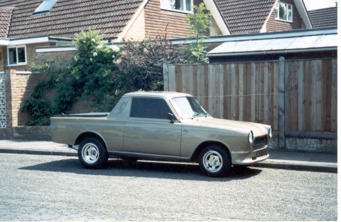 Car stuff that just doesn't happen any more - Page 25 - General Gassing - PistonHeads - This image captures a scene on a residential street. A vintage truck, painted in a light brown hue, is parked at the curb of a house with a white facade and a brick chimney. The truck has a flatbed and appears to be from the 1960s or early 1970s, judging by its style and design features. Its rear door is open, revealing the interior space inside. In front of the truck, there is a sidewalk lined with trees, adding a touch of greenery to the suburban setting. The sky overhead seems overcast, suggesting it might be a cloudy or rainy day.